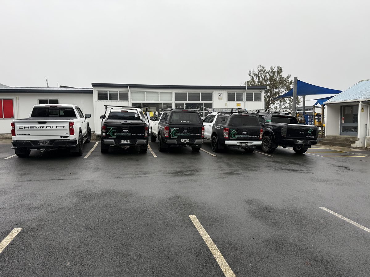 Five ZC Roofing work vehicles lined up outside a school