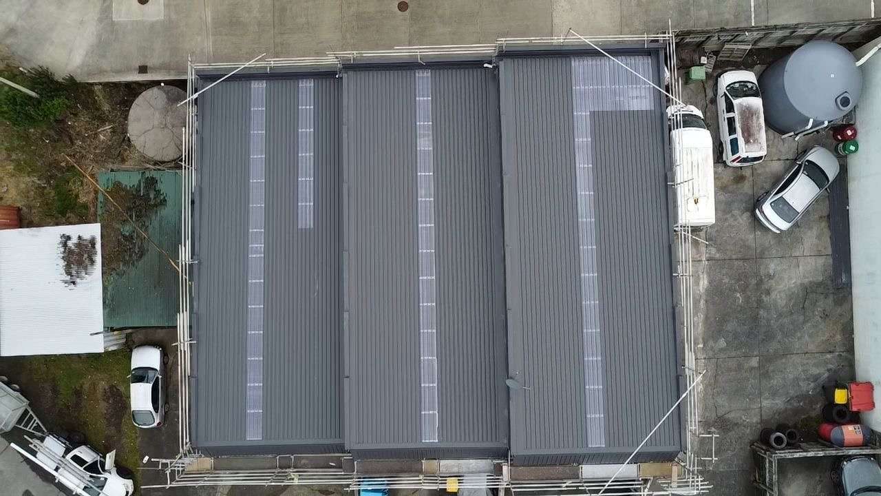 Drone photograph looking straight down on a dark grey longrun roof with clear roofing sheets, surrounded by scaffolding