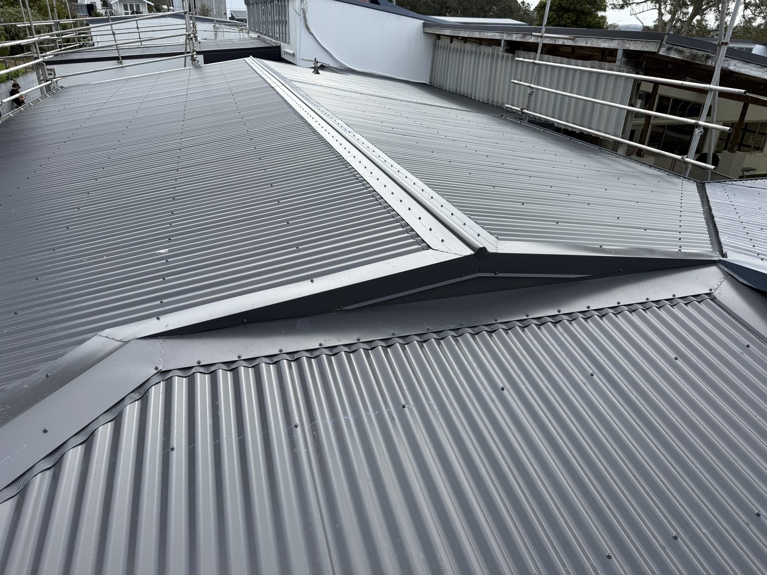 Dark grey corrugated steel roof seen from the ridge, with matching ridge, valley and apron flashings and safety rails along the edge