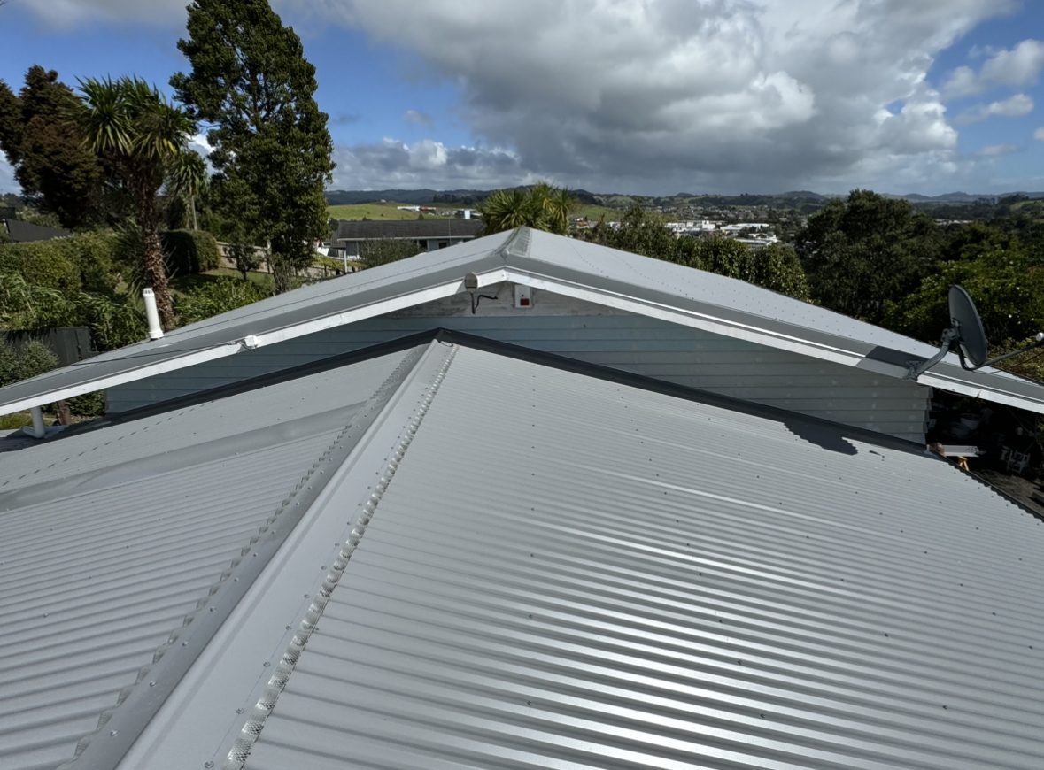 Light grey corrugated steel roof with hip capping meeting a gable with white barge boards, under a large cloud