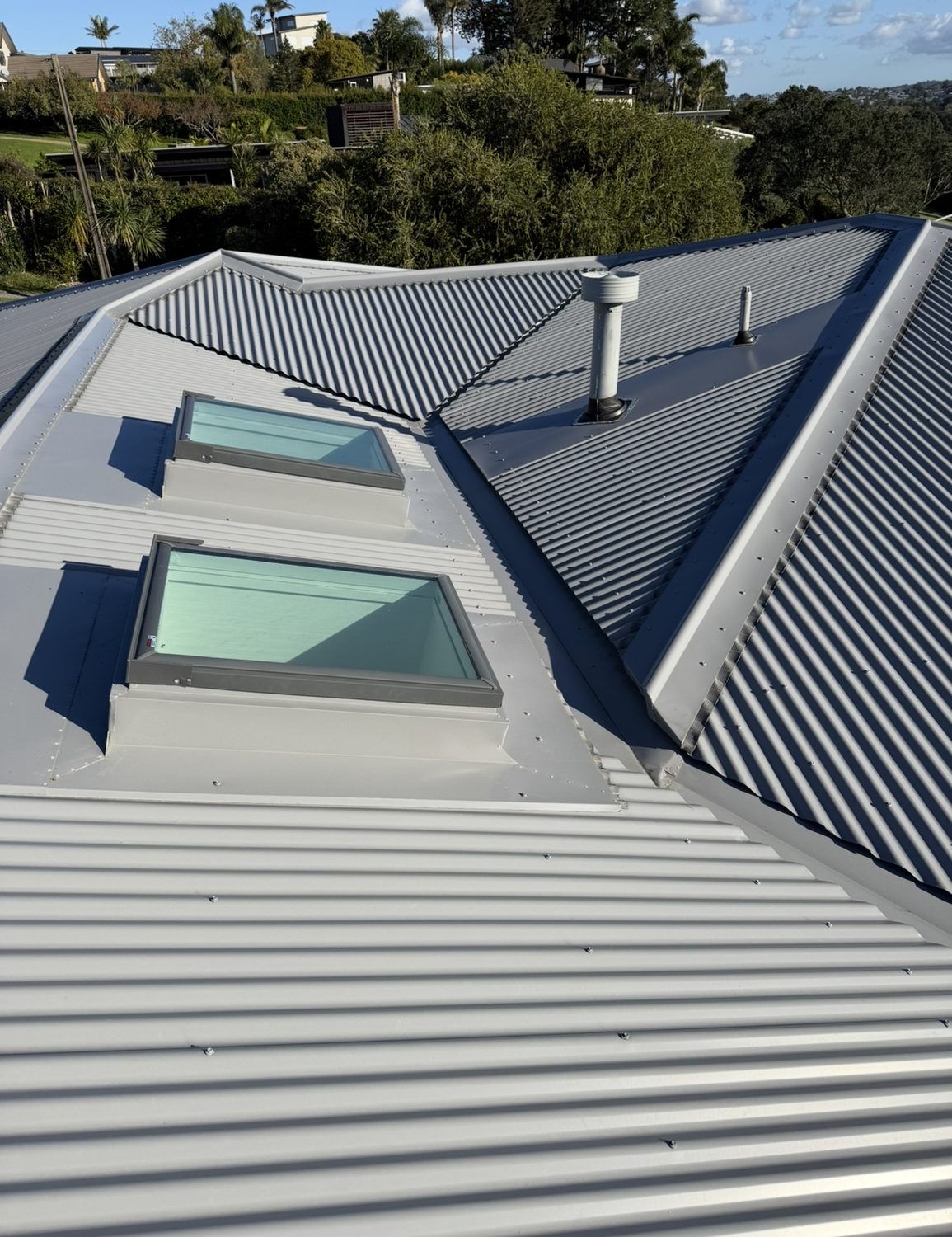 Light grey corrugated steel roof with two flat glass skylights, a flue and a valley