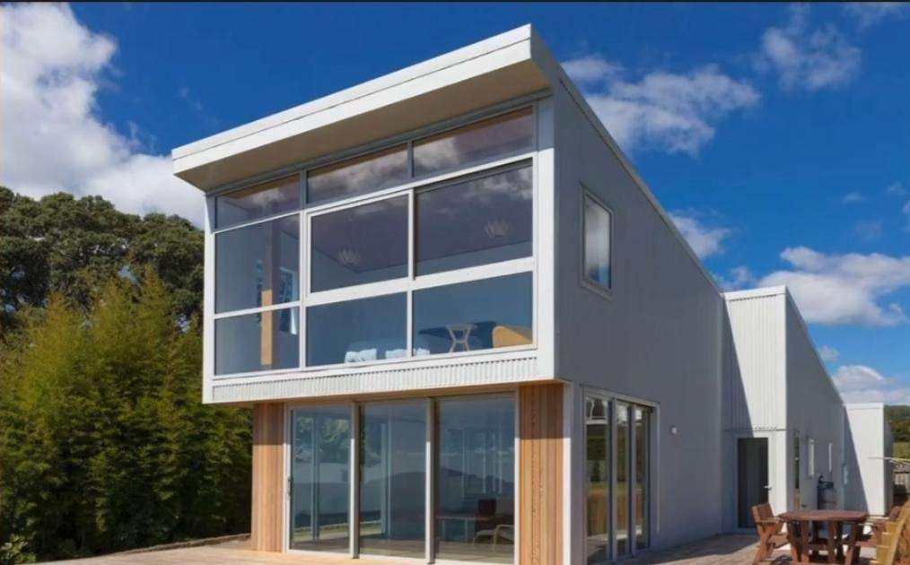 Two-storey home with a mono pitch roof, corrugated steel cladding and large windows under a blue sky