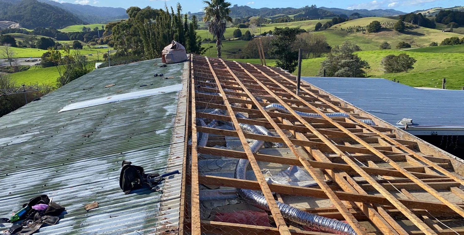 Old corrugated iron roof half stripped back to its timber purlins during a re-roof, farmland beyond