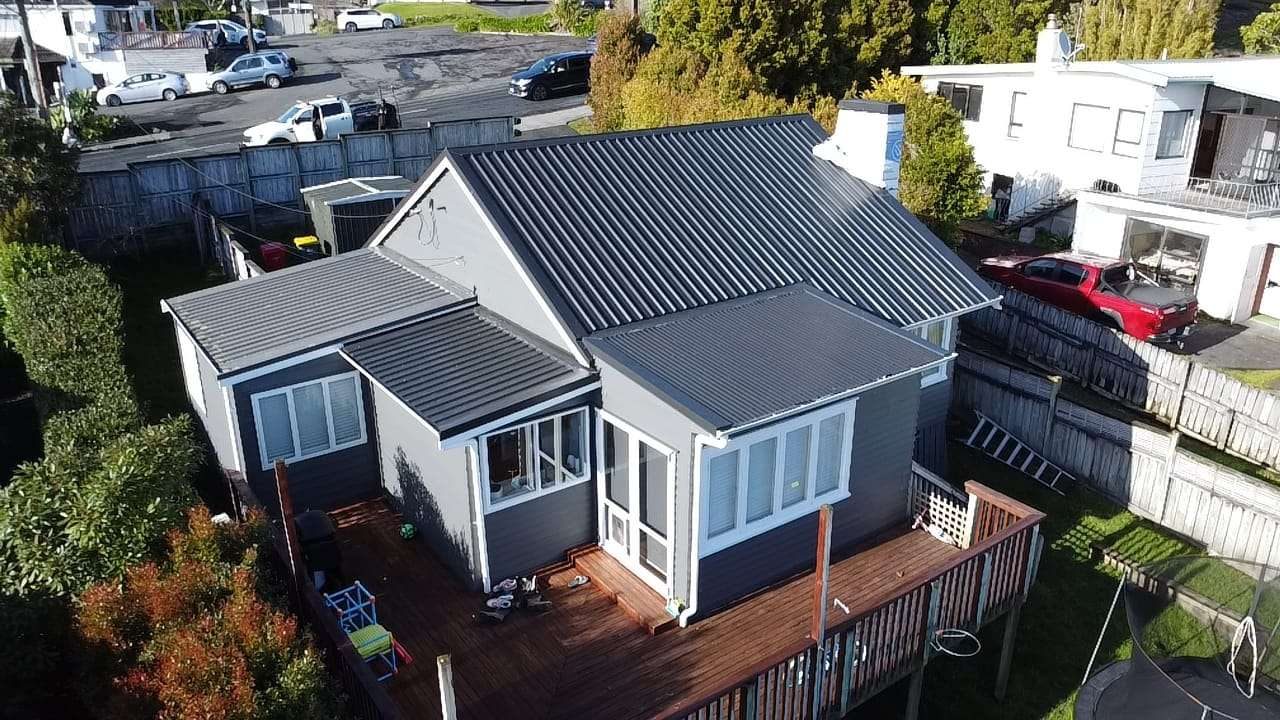 Aerial view of a weatherboard bungalow with a dark grey corrugated steel roof and a timber deck
