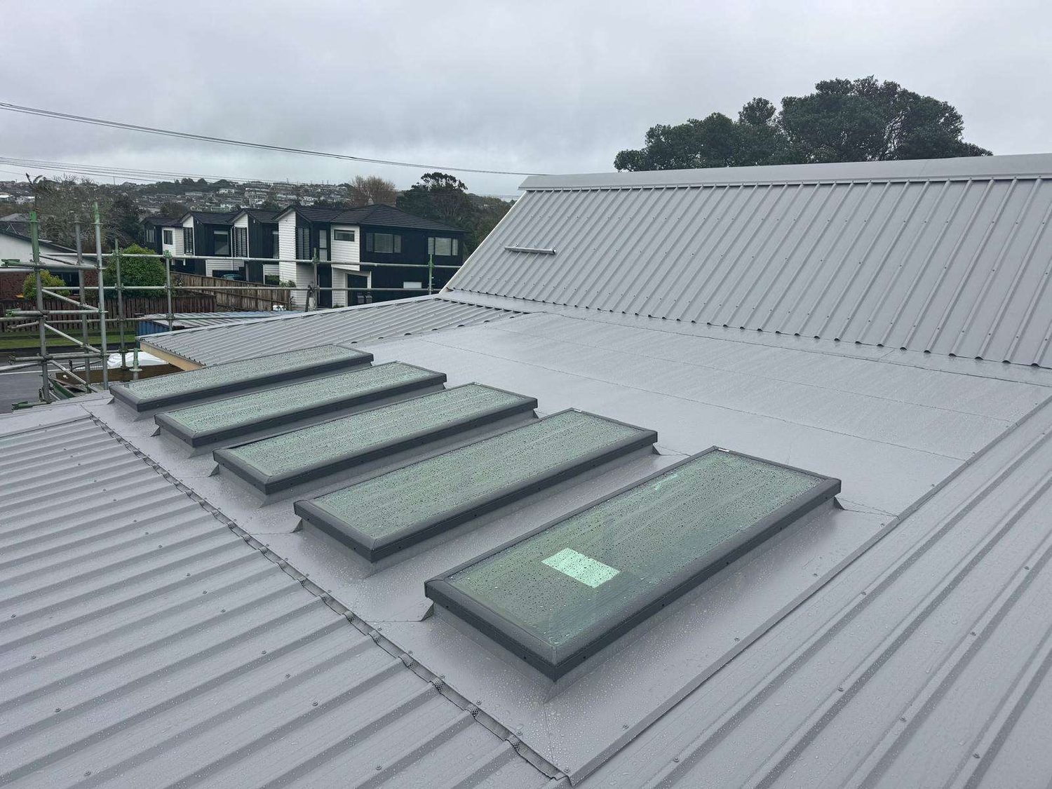 Grey longrun steel roof with a row of five skylights set into a flashed section of the roof