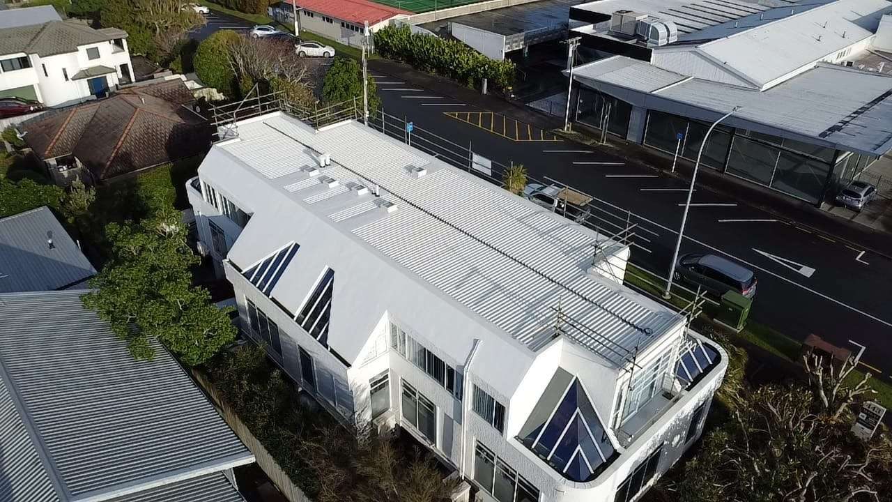 Aerial view of a white two-storey building with a white low pitch roof beside a street