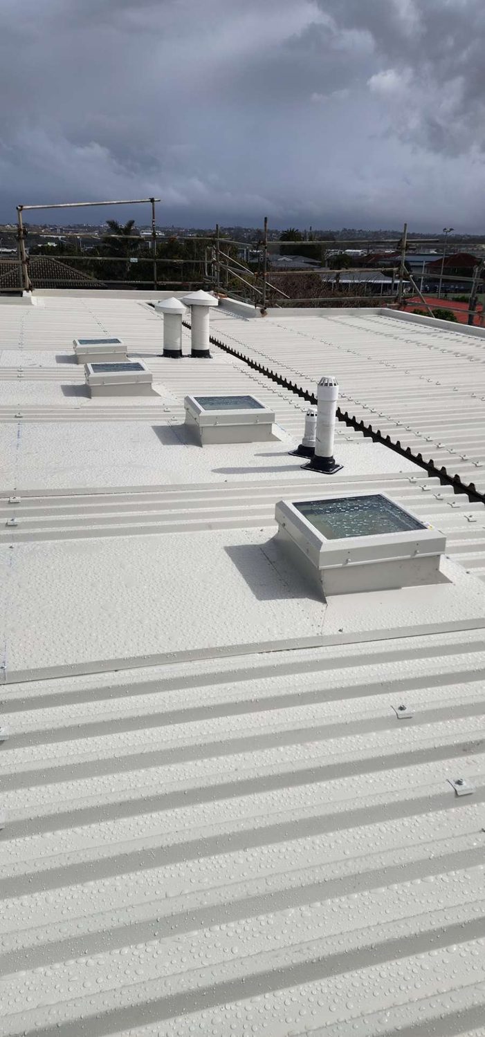 White steel roof on a commercial building with square skylights and roof vents under a stormy sky