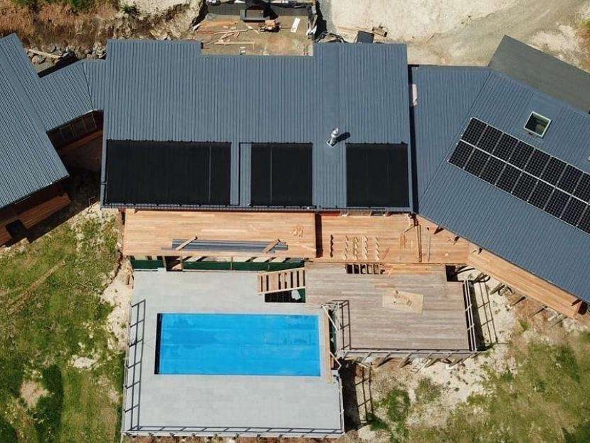 Aerial view of a new timber-clad home with dark grey longrun roofing, solar panels and a swimming pool