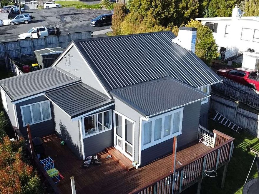 Aerial view of a weatherboard bungalow with a dark grey corrugated steel roof and a timber deck