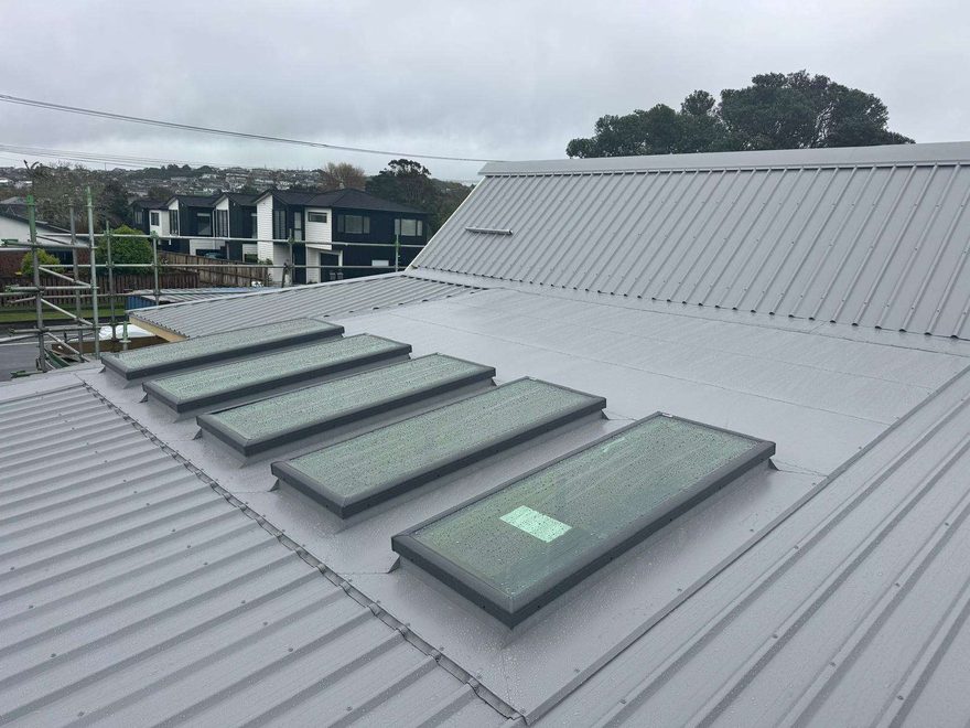 Grey longrun steel roof with a row of five skylights set into a flashed section of the roof